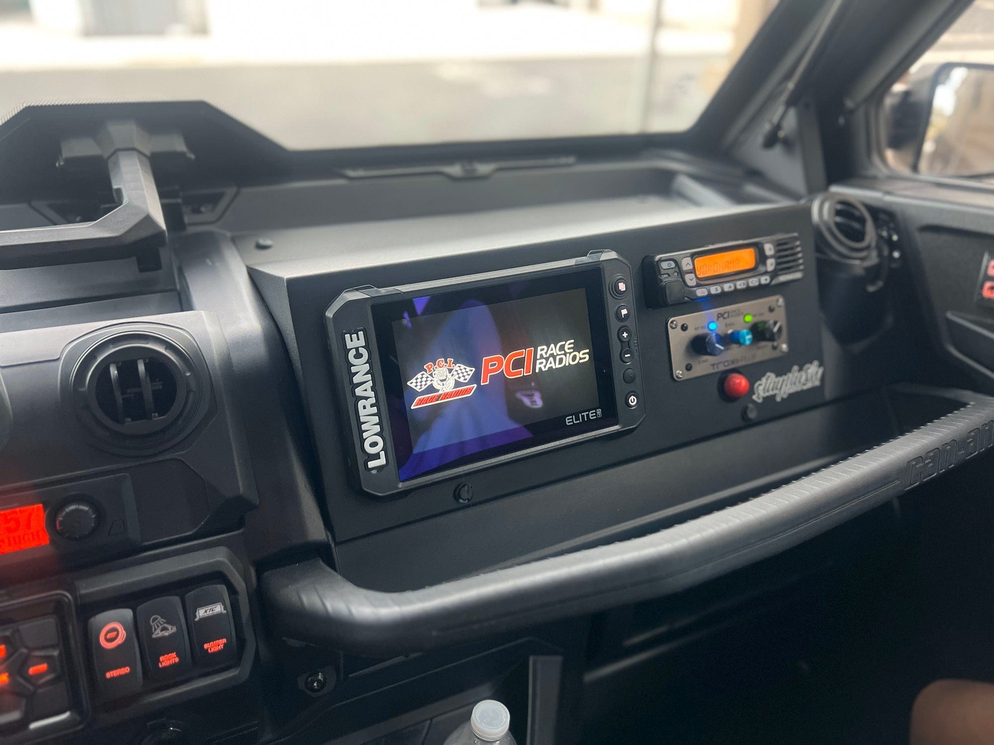 Dashboard of an off-road vehicle with a Custom Defender Glove Console by StayFlush, featuring a Lowrance Elite display showing the PCI Race Radios logo, multiple switches, a communication radio, dash accessories, and a bottle holder.