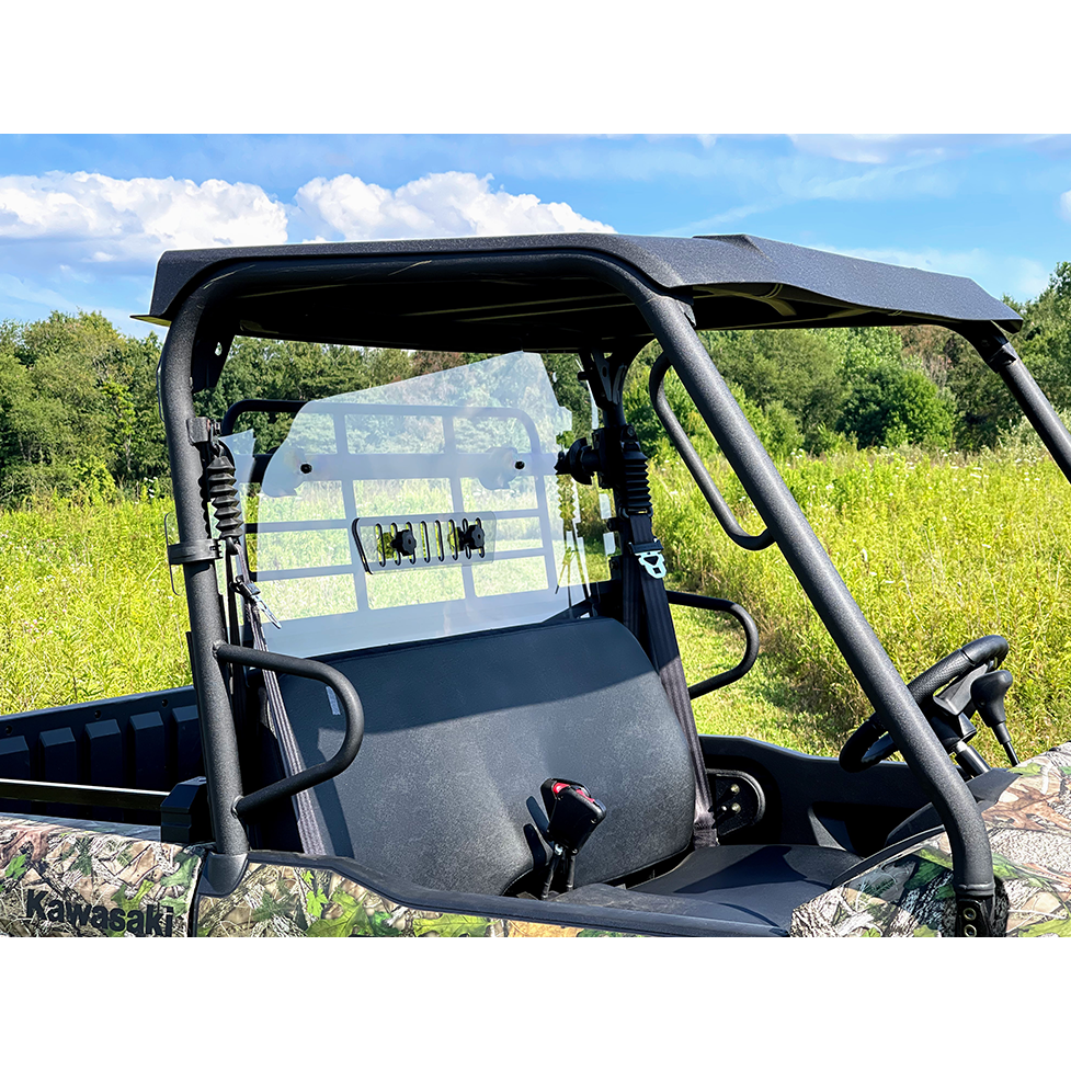 A Kawasaki Mule Pro-MX with a Spike Vented Clear Rear Windshield is parked on grass under a blue sky with scattered clouds, framed by trees in the background.