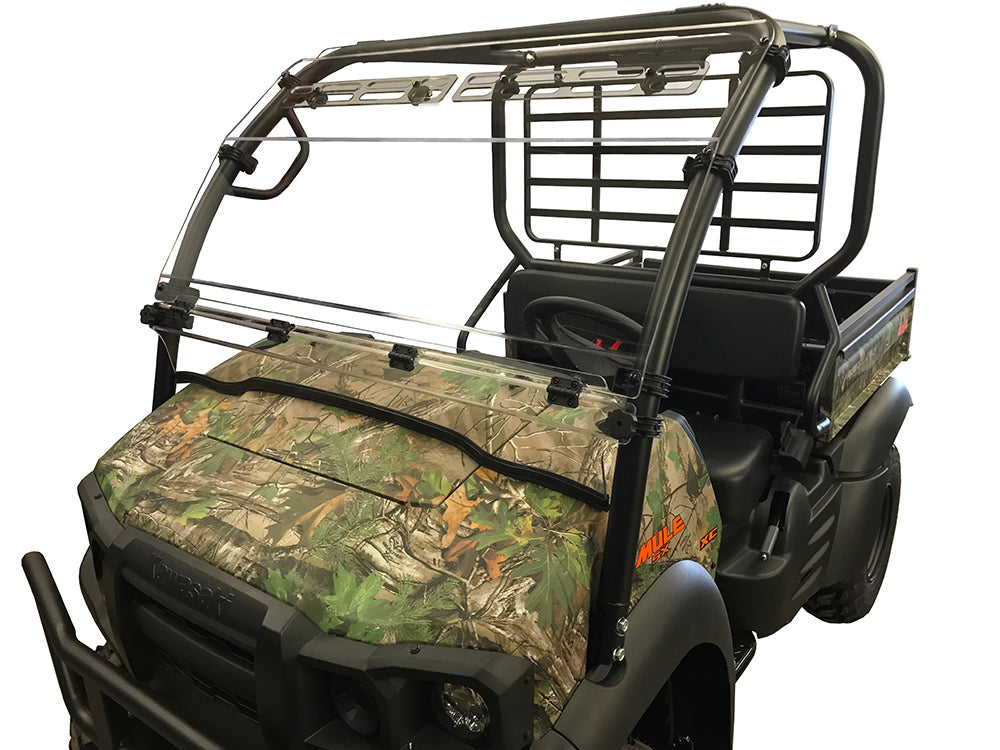 A Kawasaki Mule SX with a camouflage pattern features a clear Spike folding windshield for protection, a black metal roll cage, two seats, and an open rear cargo bed.