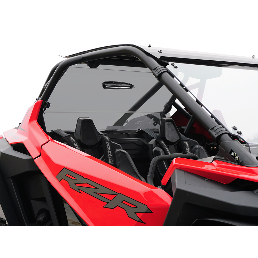 A close-up of a red RZR off-road vehicle with black seats and a Spike Polaris RZR Pro Xp Turbo rear tinted windshield with tool-less rapid release, showing part of the interior and roll cage.