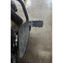Close-up of the Adjustable Foot Rest Kit Beveled Style by Witchdoctors, featuring large grooved rubber footrests and adjustable pegs on a concrete floor. The design enhances motorcycle comfort. A rear wheel is partially visible in the background.
