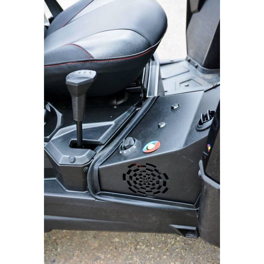 Close-up of a black UTV’s seat and controls, highlighting the gear shift, rotary dial, buttons, and speaker grille. Textured footrest, seat edge, and durable polycarbonate door panels are shown near the Open Trail UTV Cab Heater.
