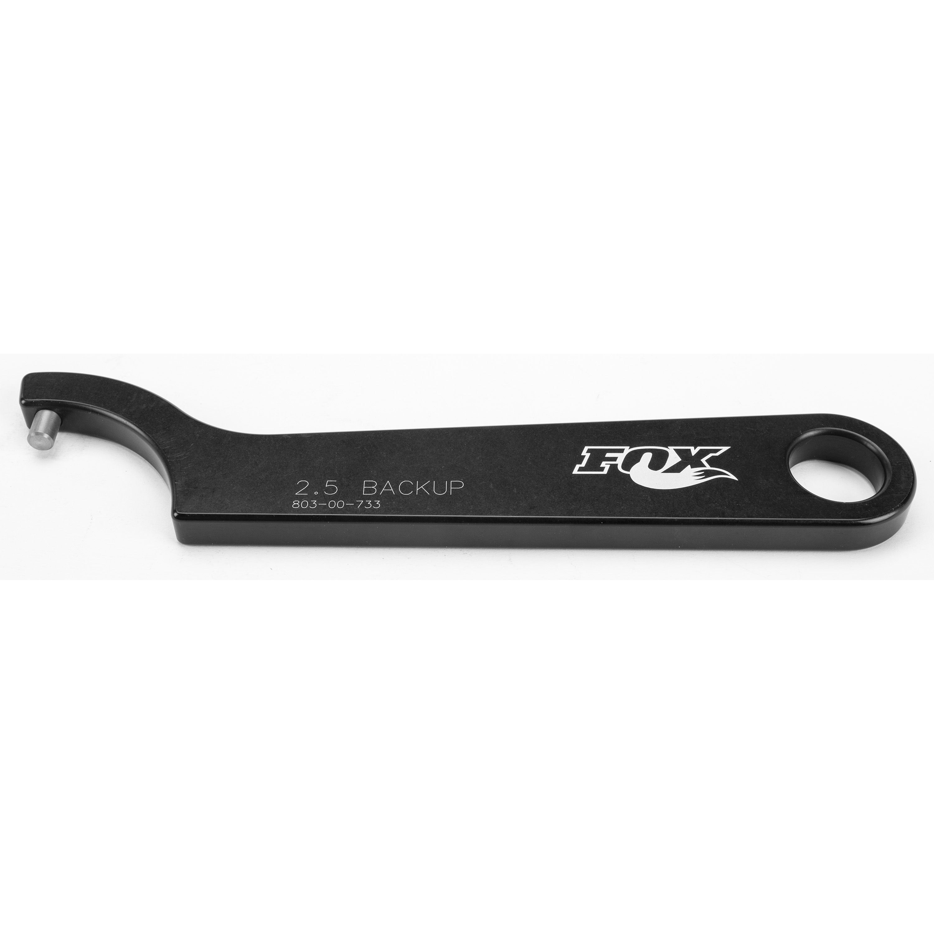 The Spanner Wrench 2.5 Backup by Fox is a black metal tool (803-00-733) with the FOX logo, featuring a hooked end with a pin and a hole at the other end, designed for suspension maintenance.