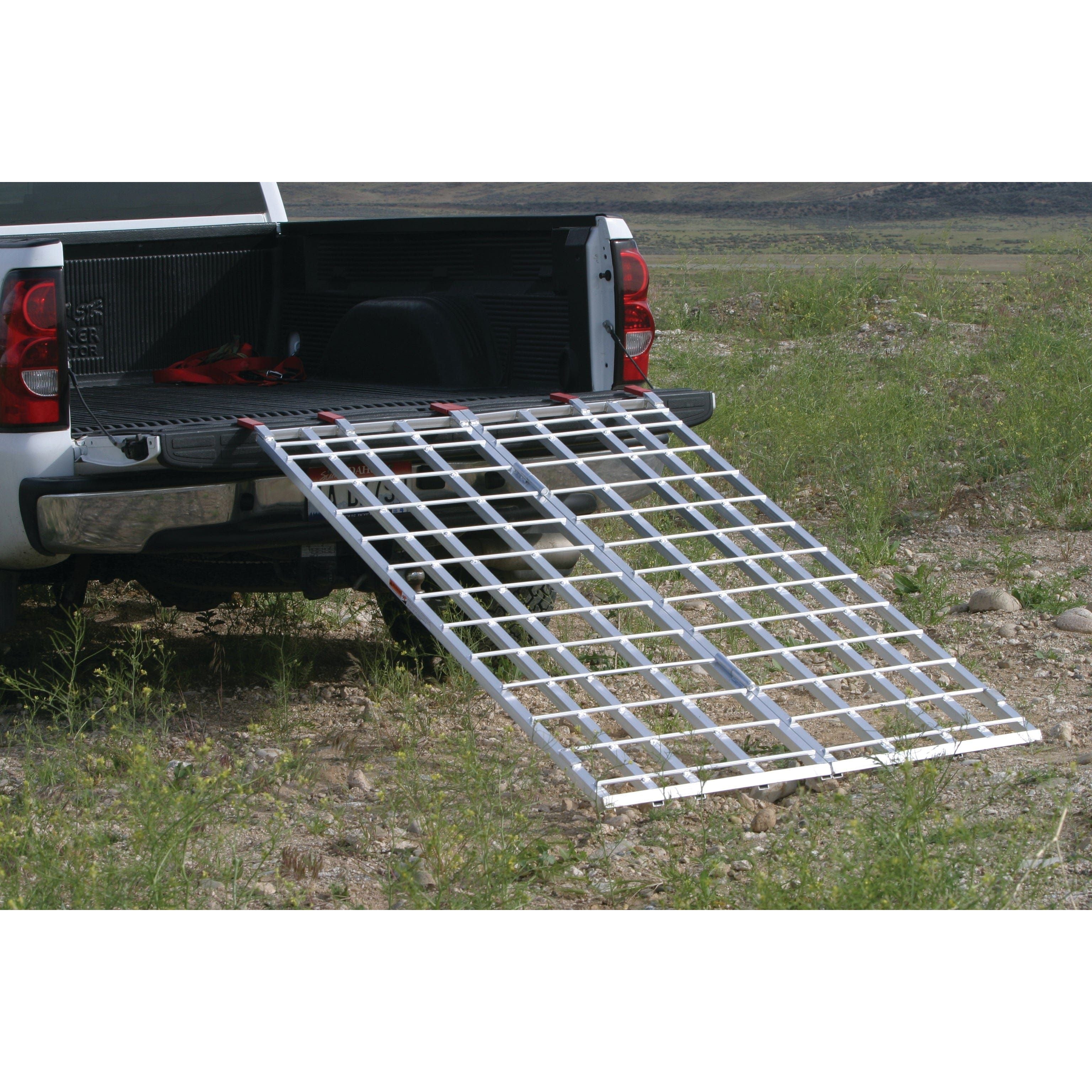 The Aluminum Bi-Fold Ramp 1200 Lbs 70 X 48 by Open Trail attaches to a pickup’s open tailgate, extending to uneven ground. Its wide, grid-patterned aluminum design provides traction for safe, easy loading in outdoor settings.