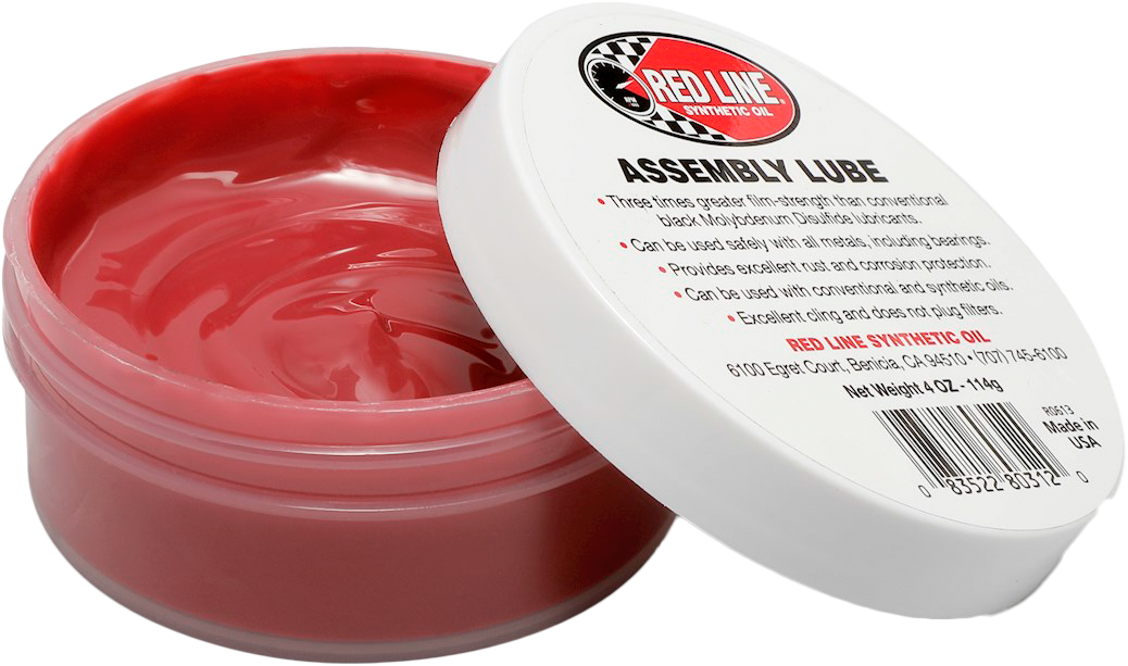 An open container of Assembly Lube 4Oz by Red Line, showing its pinkish-red high film strength lubricant, with a white lid displaying product details resting on the edge.