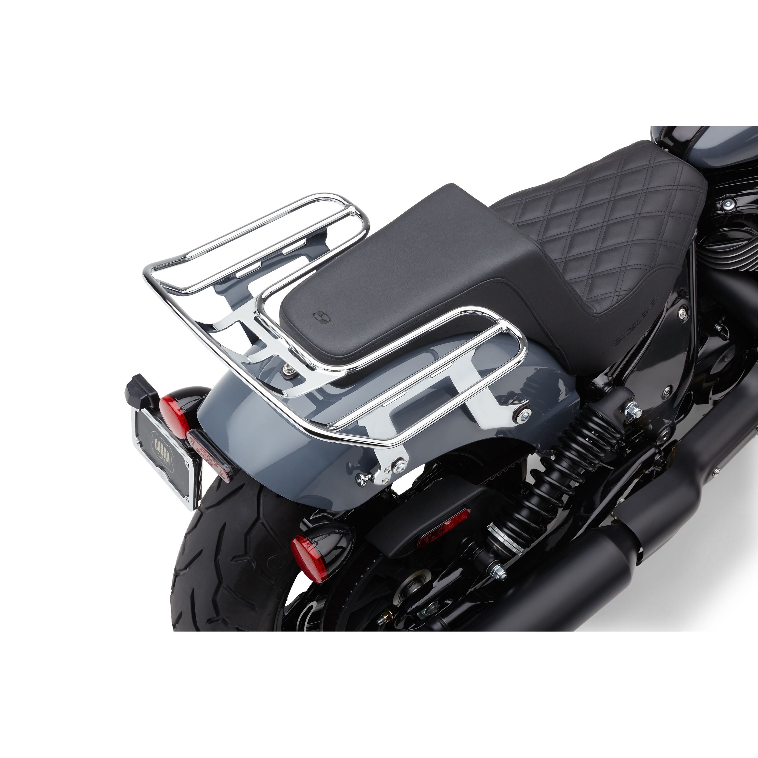 A close-up of a motorcycle's rear shows a quilted black seat, Detachable Big-Ass Luggage Rack 2-Up Chrome for Indian Chief 22-24 by Cobra, rear suspension, tire, and license plate on a gray fender.