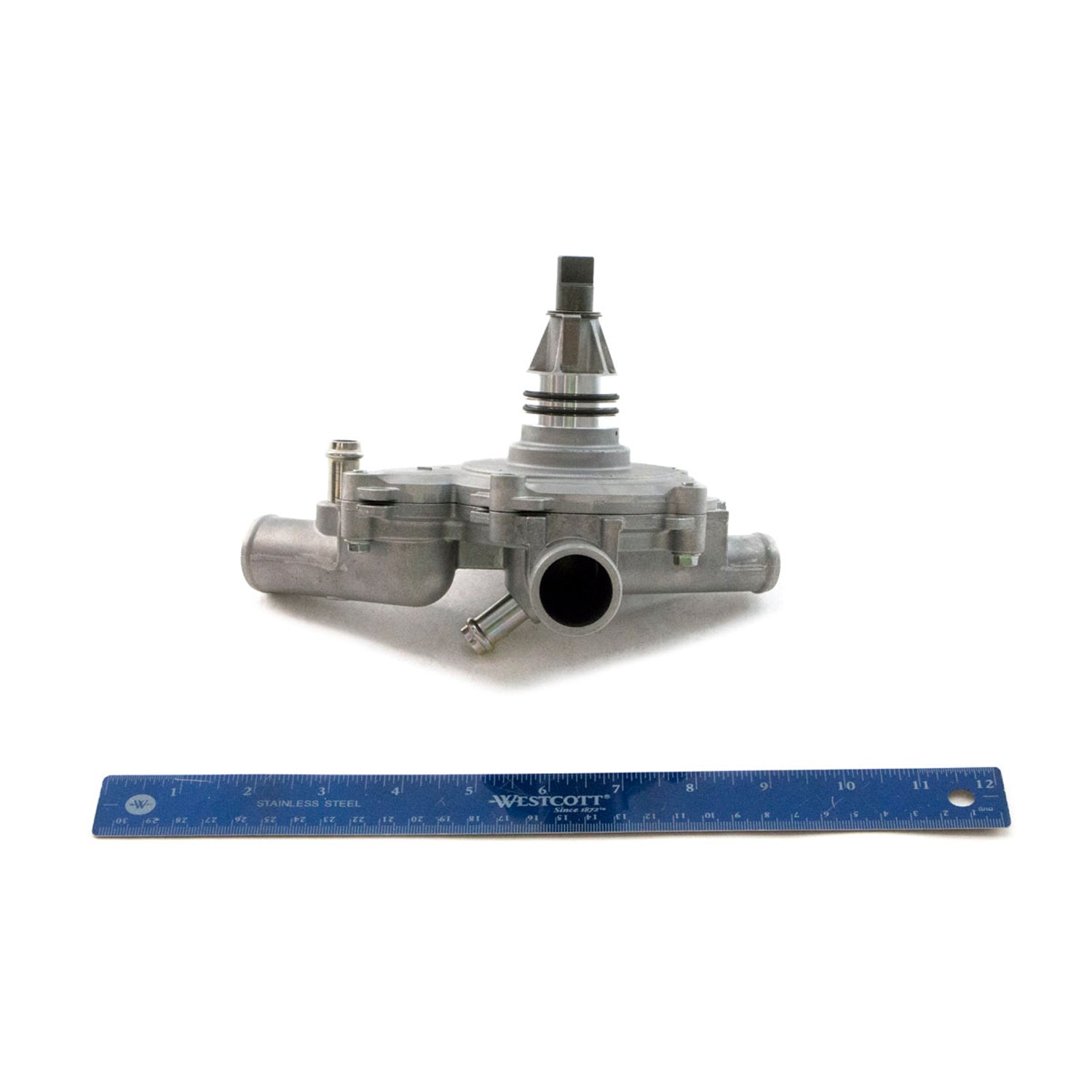 Silver metal water pump with central shaft and multiple inlet/outlet ports, alongside blue ruler for scale.