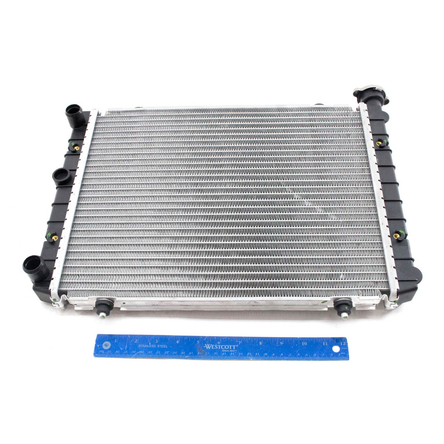 Silver aluminum radiator with black plastic tanks on sides, rectangular shape, blue ruler below for scale.