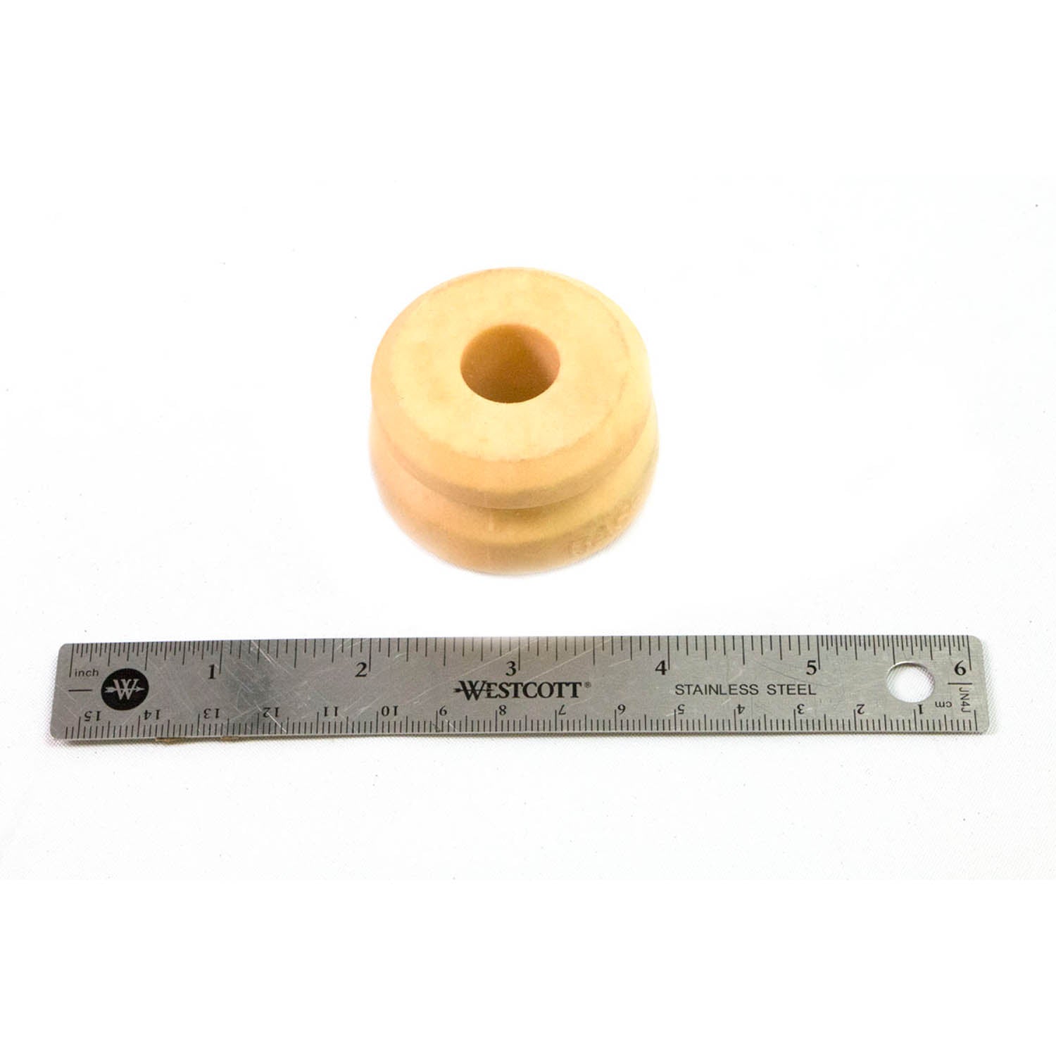 Beige cylindrical rubber bump stop with a central hole, shown next to a 6-inch metal ruler for scale.