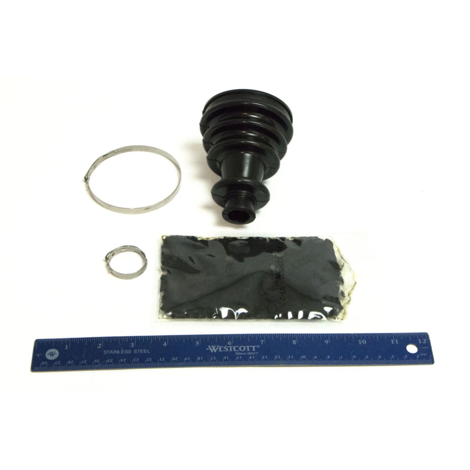 Black rubber CV joint boot with two metal clamps and grease pack, shown next to a blue 12-inch ruler for scale.