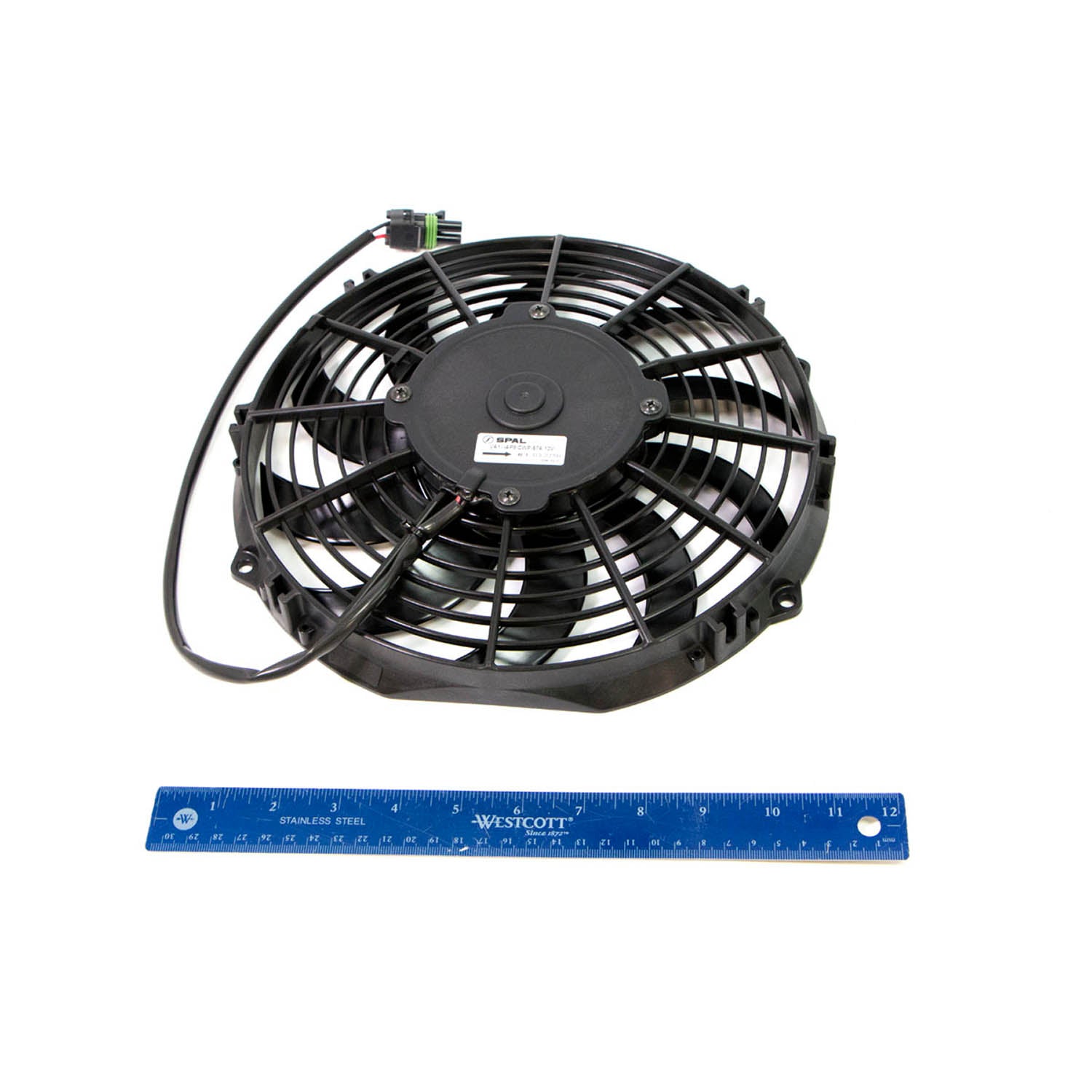 Black circular electric cooling fan with multiple blades and attached wiring harness next to a 12-inch blue ruler.