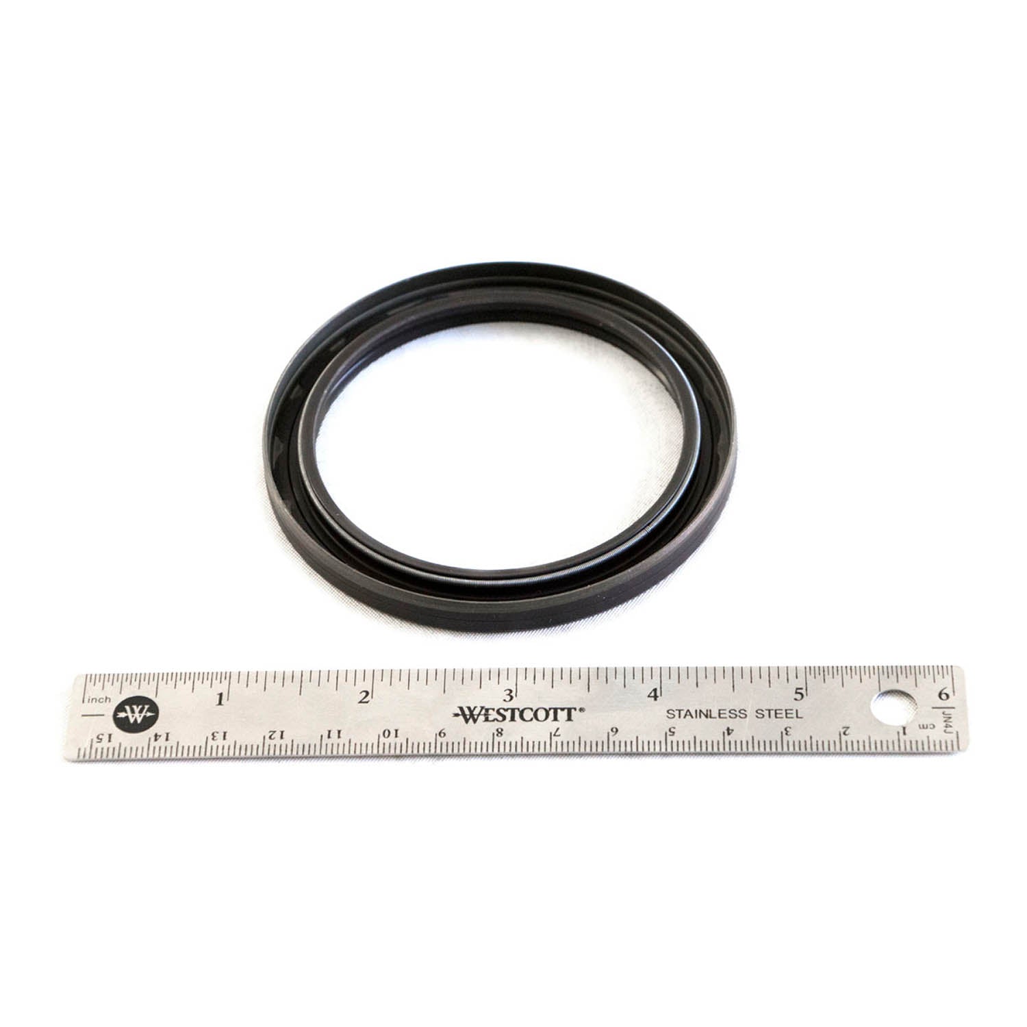 Black rubber oil seal with smooth outer edge and inner lip, placed above a 12-inch metal ruler for scale.