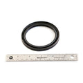 Black rubber oil seal with smooth outer edge and inner lip, placed above a 12-inch metal ruler for scale.