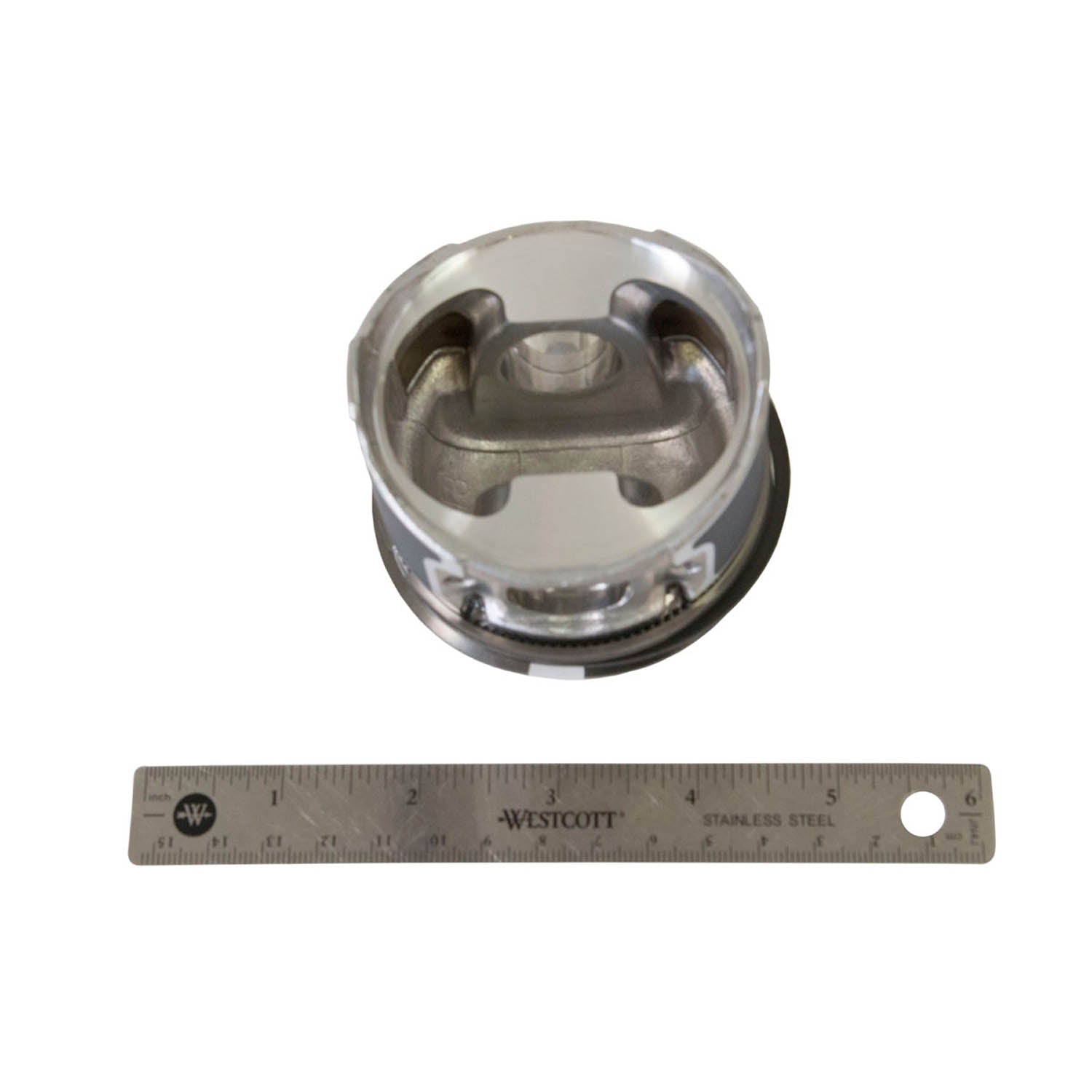 Silver metallic piston with two valve cutouts and grooved sides next to a 6-inch metal ruler.