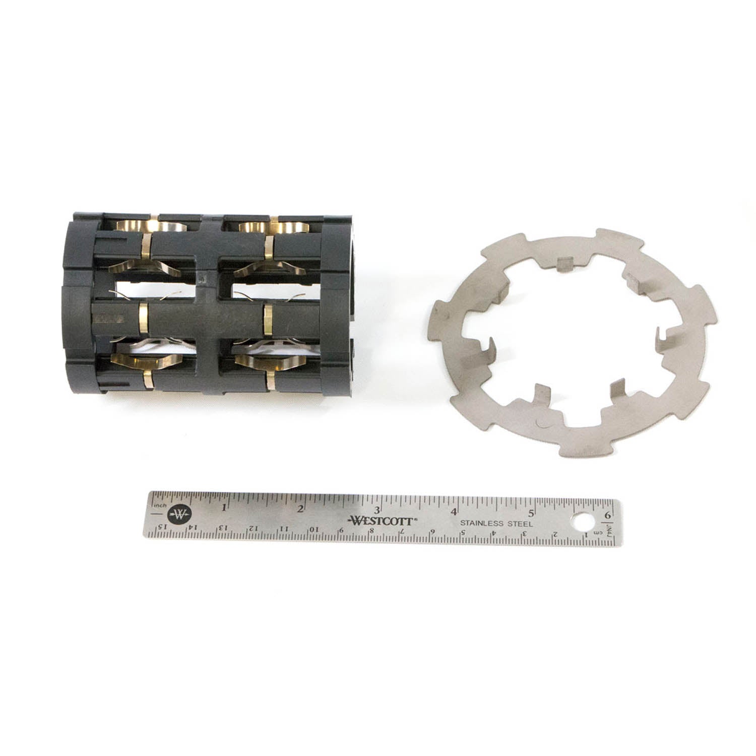 Black cylindrical gearcase roller cage with metal pins and circular gray metal retaining clip next to a 6-inch metal ruler.