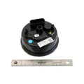 Round black plastic speedometer housing with electrical connectors and barcode labels, next to a 12-inch ruler for size.
