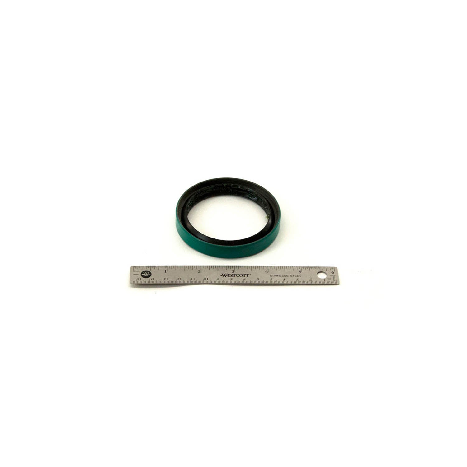 Black and green circular front hub seal with rubber material next to a metal ruler for size reference.
