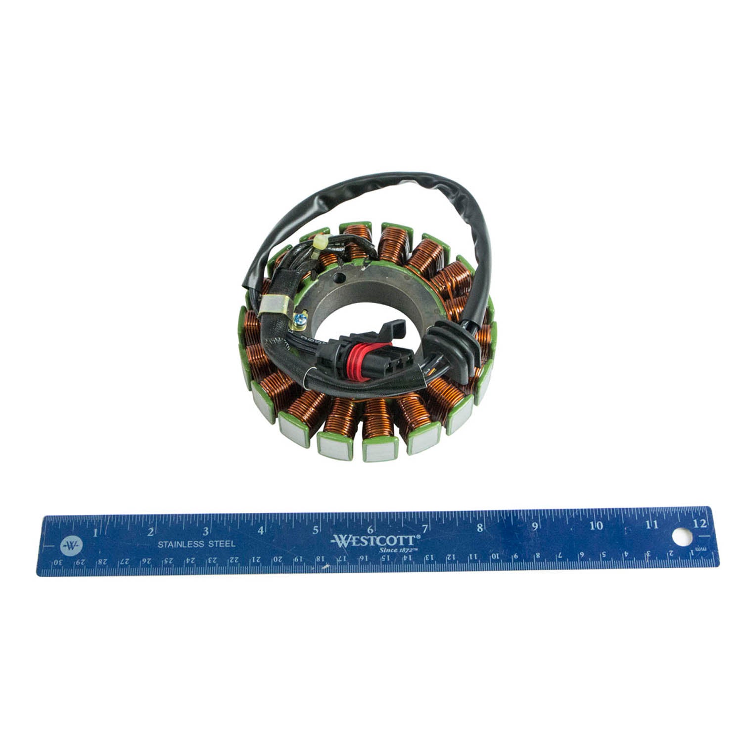 Circular copper coil stator with black wiring harness and connector, next to a 12-inch blue ruler for scale.