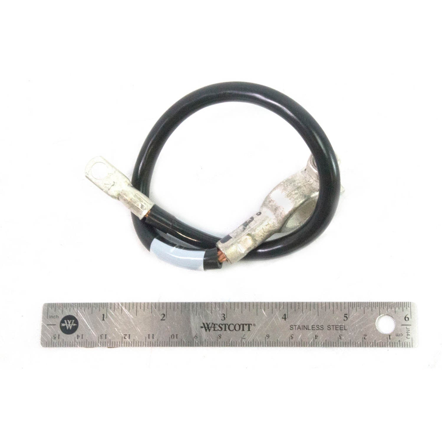 Black insulated battery to ground cable with metal terminal connectors on each end, shown with a metal ruler for scale.