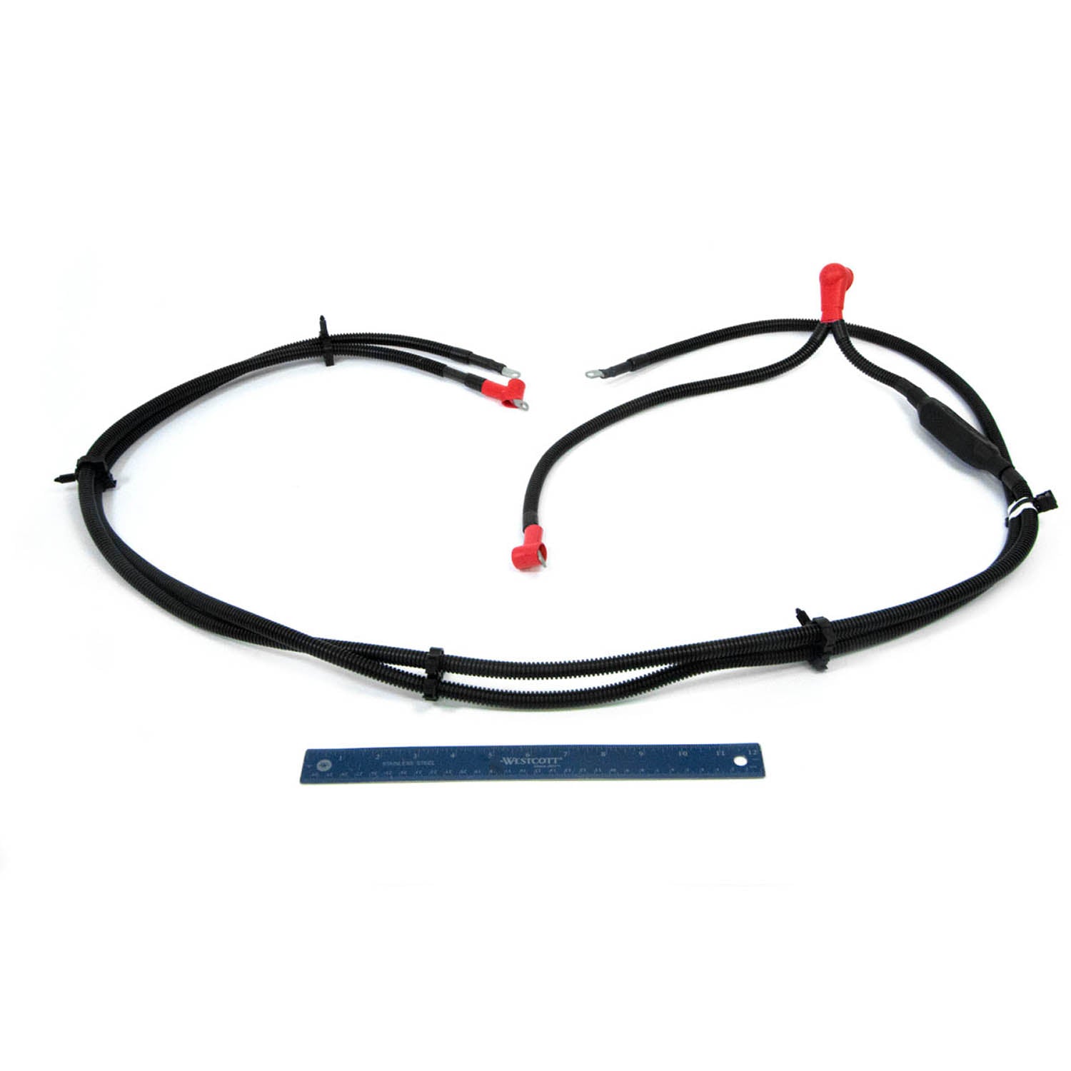 Black insulated battery ground cable with red terminal covers and secured connectors, laid flat next to a blue ruler for.