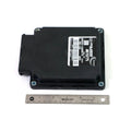 Black rectangular electronic control module with connector port and attached label above a 6-inch ruler.
