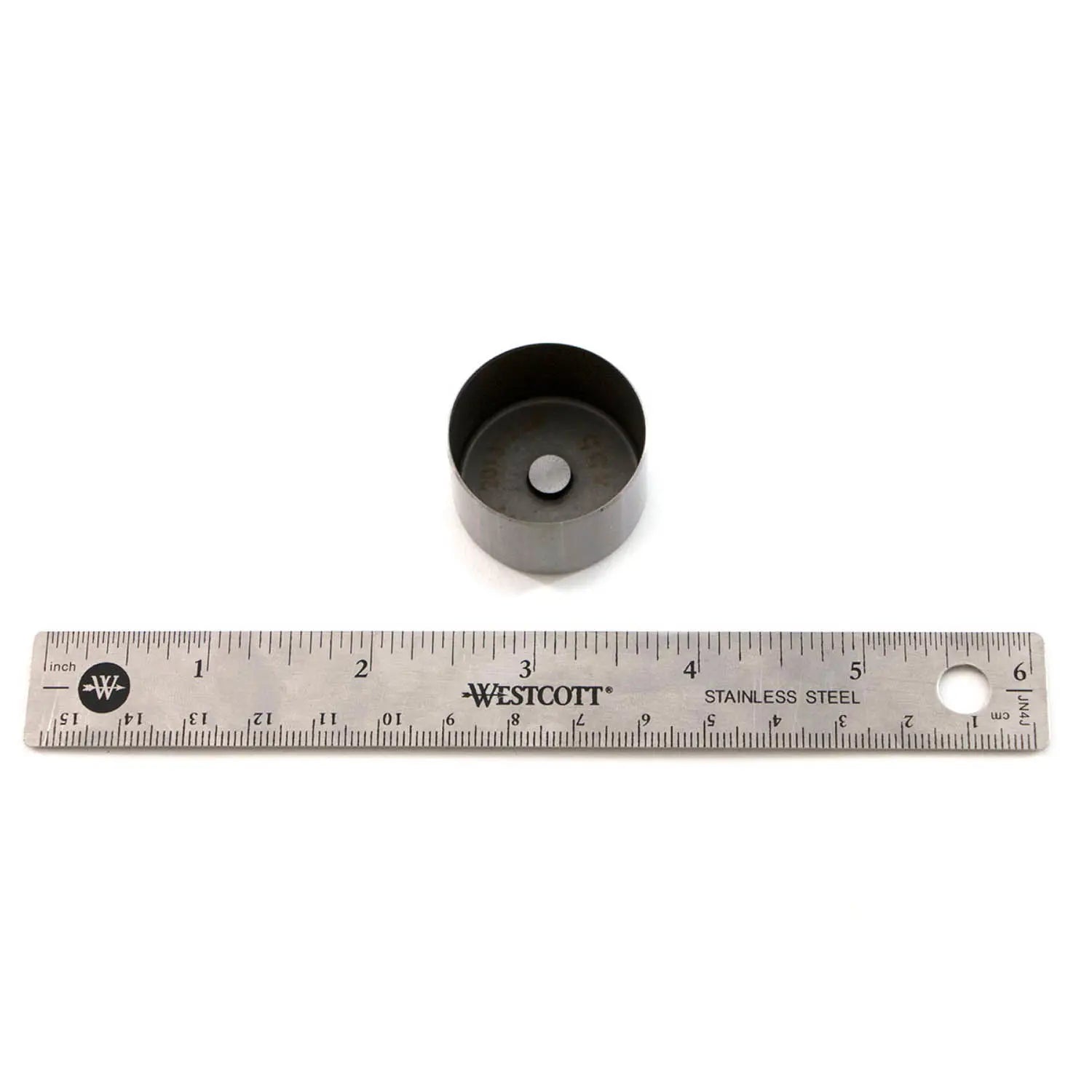 Black cylindrical metal valve tappet with recessed center, next to 6-inch stainless steel ruler.