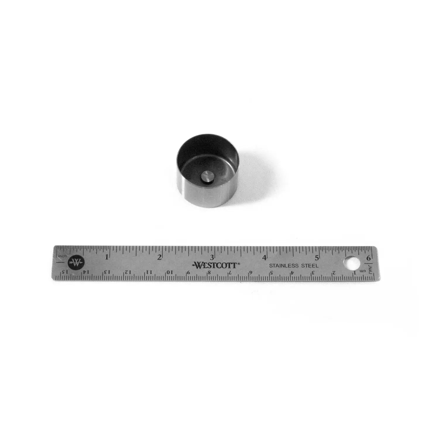 Small cylindrical metal valve tappet with hollow center beside a 6-inch stainless steel ruler displaying inch measurements.