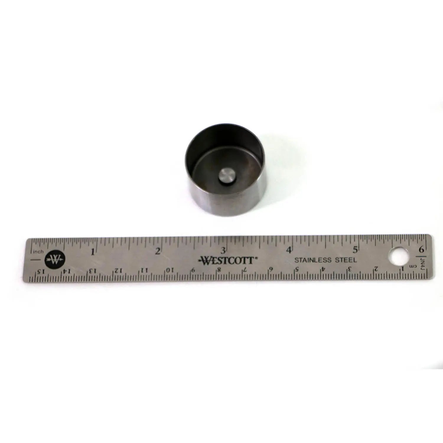 Round black metal valve tappet next to a 6-inch stainless steel ruler on white background.