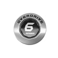 Silver round motorcycle cam cover with black center labeled "Overdrive 6 Speed".