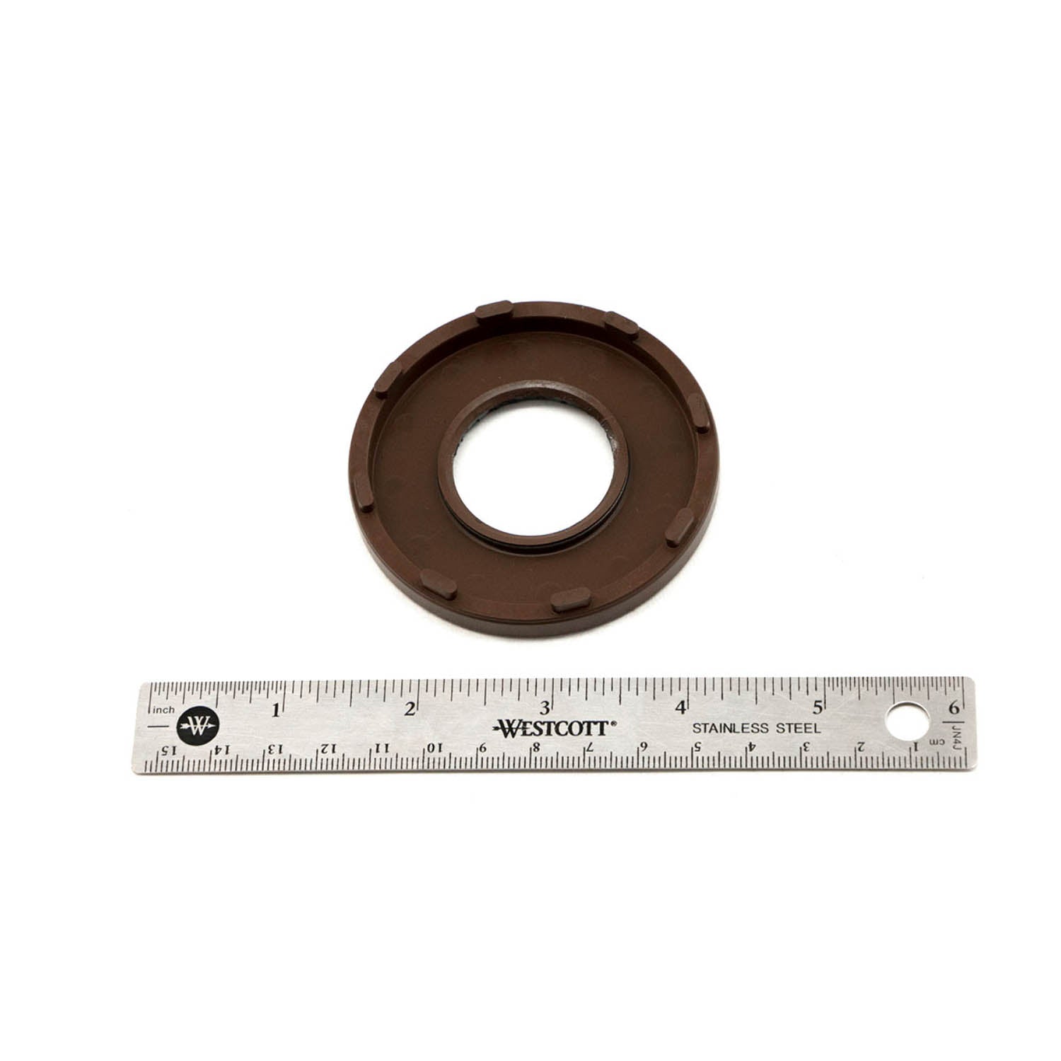 Brown circular crankshaft seal with inner lip and ridged outer edge, next to a 6-inch stainless steel ruler.