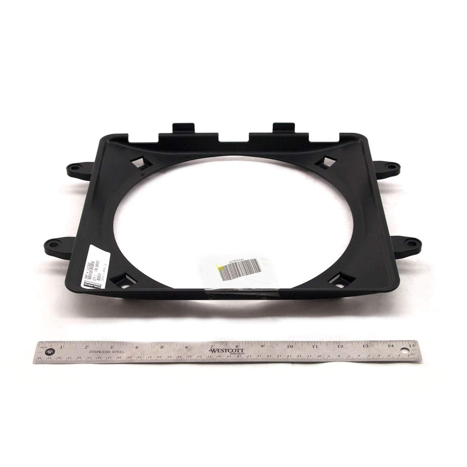 Black rectangular plastic fan shroud with central circular opening and mounting tabs, shown with metal ruler for scale.