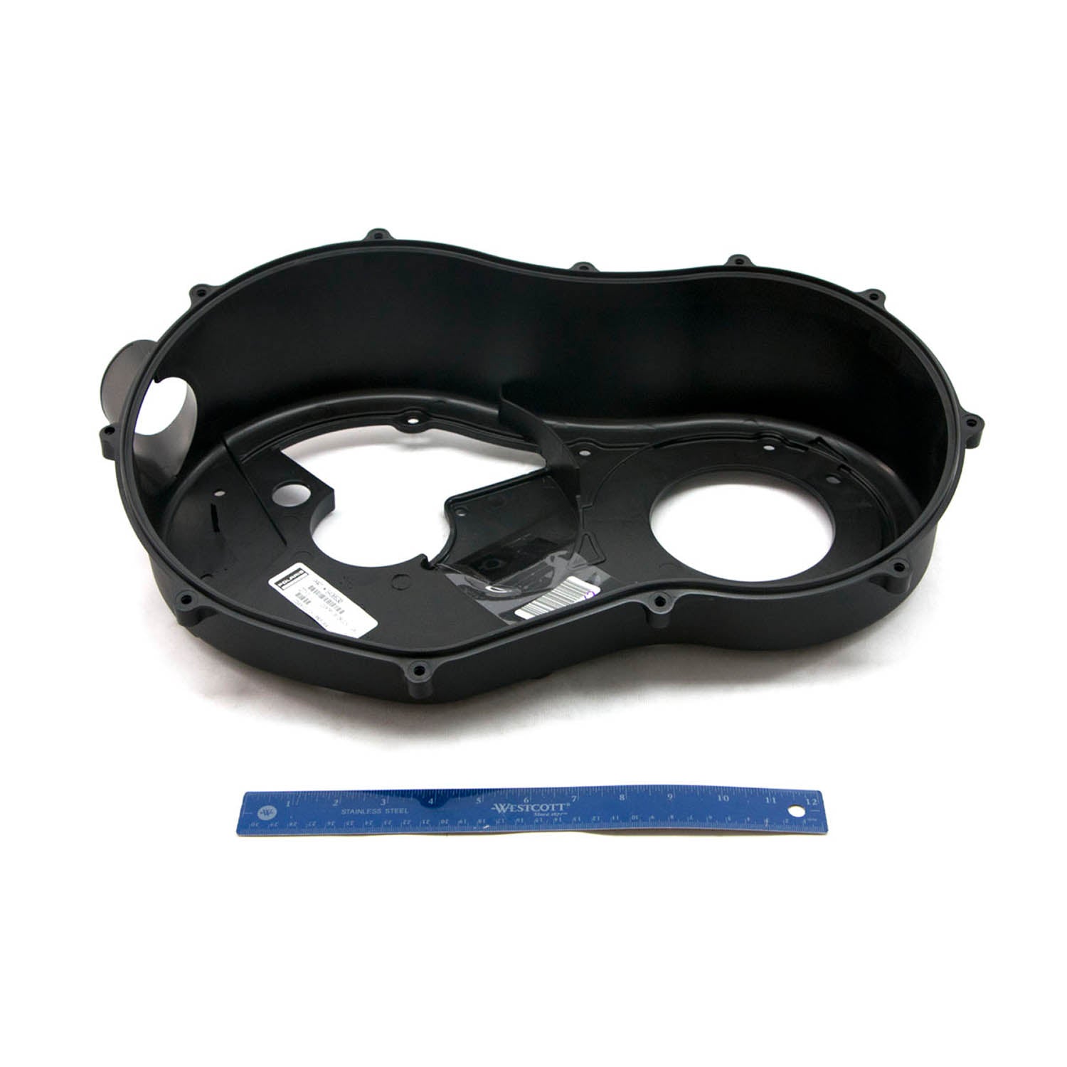 Black molded plastic inner clutch cover with multiple bolt holes and circular cutouts, placed next to a blue ruler for scale.