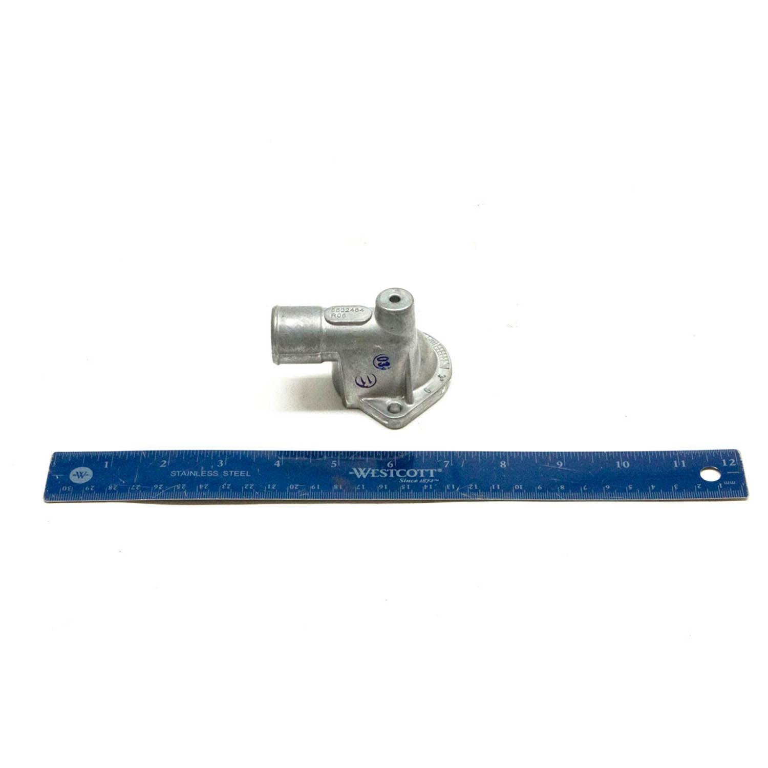 Silver cast metal thermostat cover with a tubular outlet and mounting holes next to a 12-inch blue ruler.