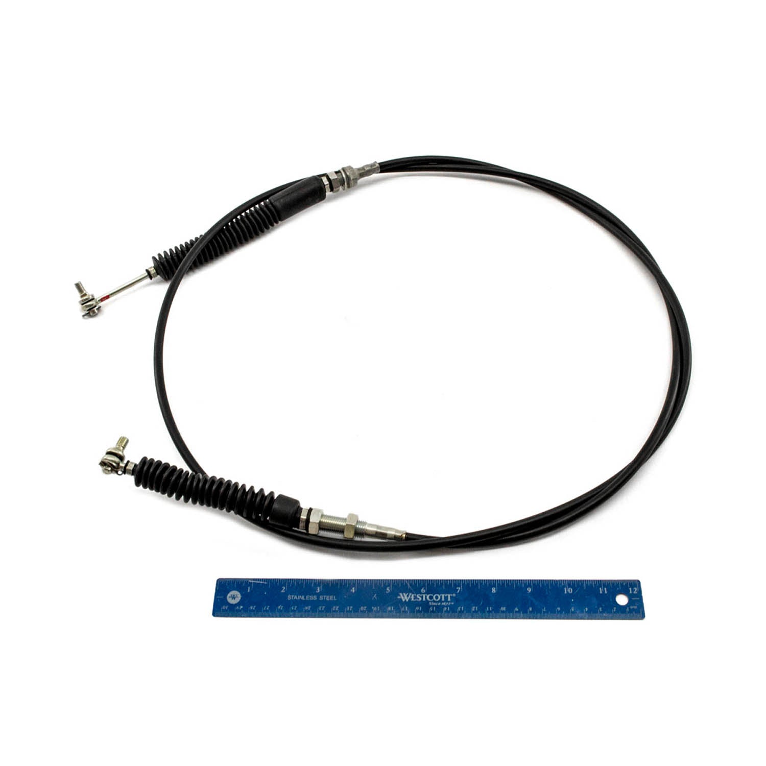 Black flexible shift cable with metal connectors and protective rubber boots, shown with blue ruler for scale.