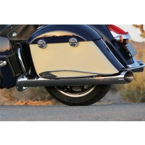 Close-up side view of a motorcycle’s rear wheel, chrome exhaust pipe, and beige saddlebag accented by the Pinnacle Saddlebag Protector Rail, Chrome, Pair by Polaris, parked on a road with blurred outdoor scenery in the background.