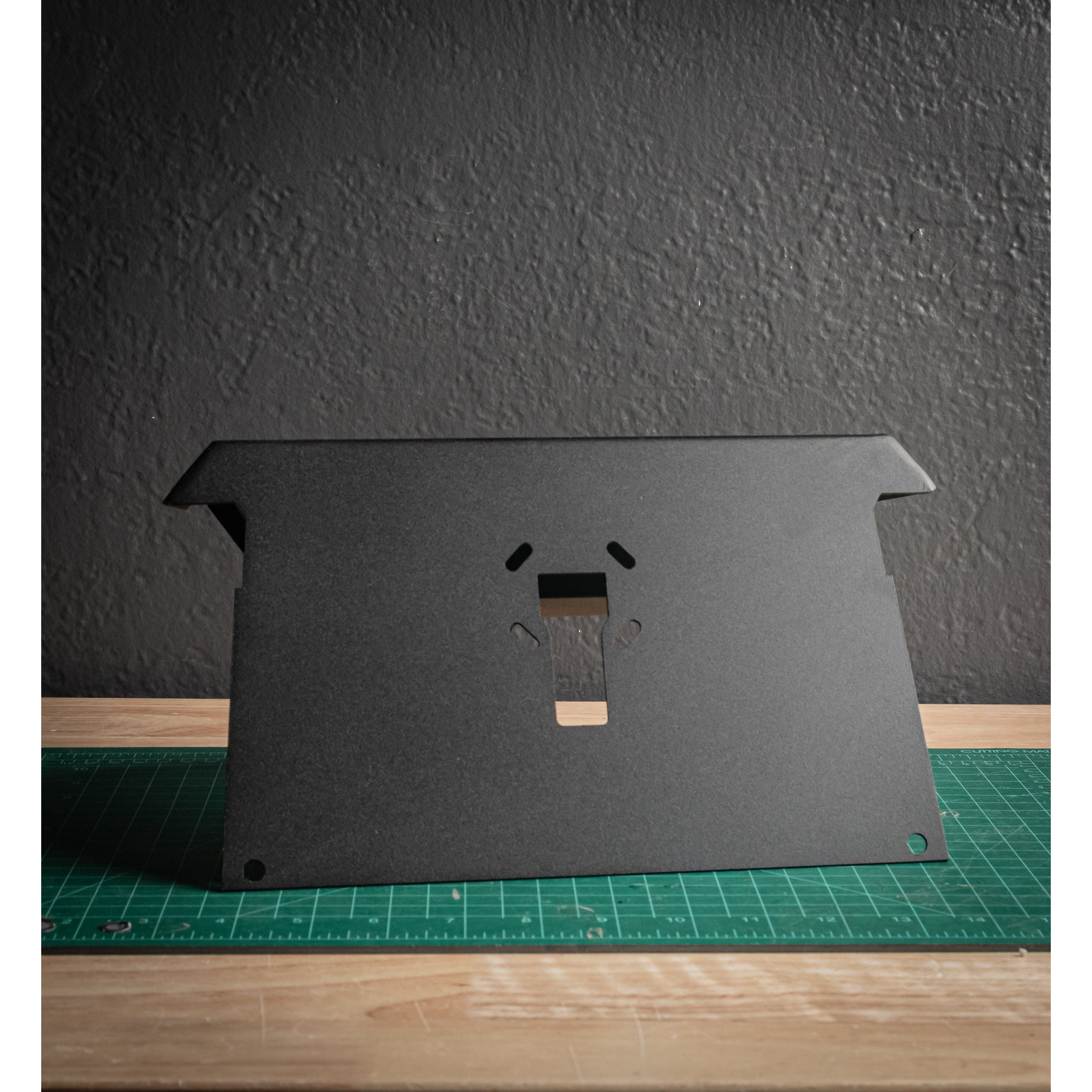 The Turbo S Universal Tablet/Garmin Mount by StayFlush in black features a center cutout and stands upright on a green cutting mat atop a wooden table, set against a textured dark gray wall for a clean, factory look.