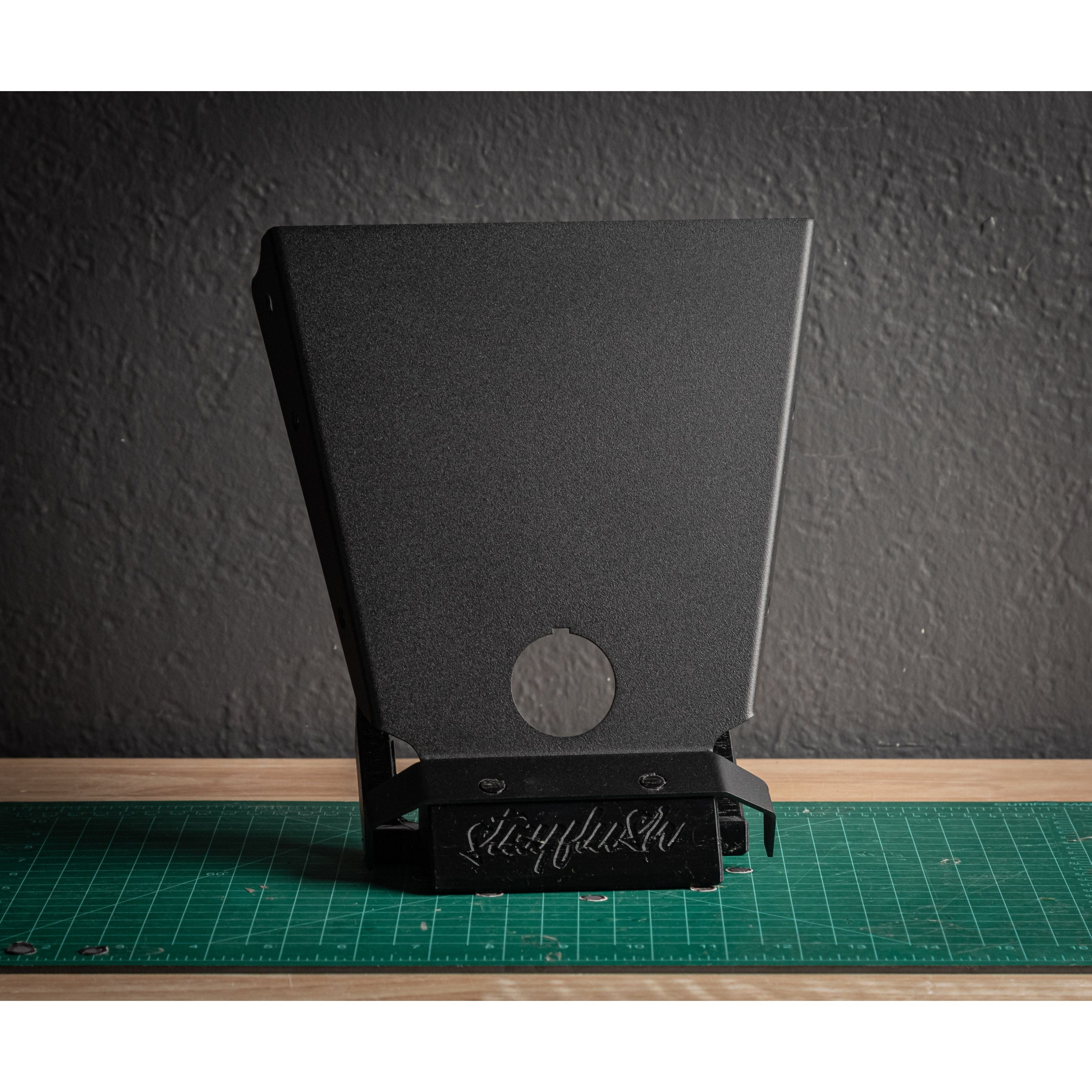 A black, angular StayFlush Clean Start Console by StayFlush with a circular cutout stands upright on a green cutting mat, set against a textured dark gray wall background.