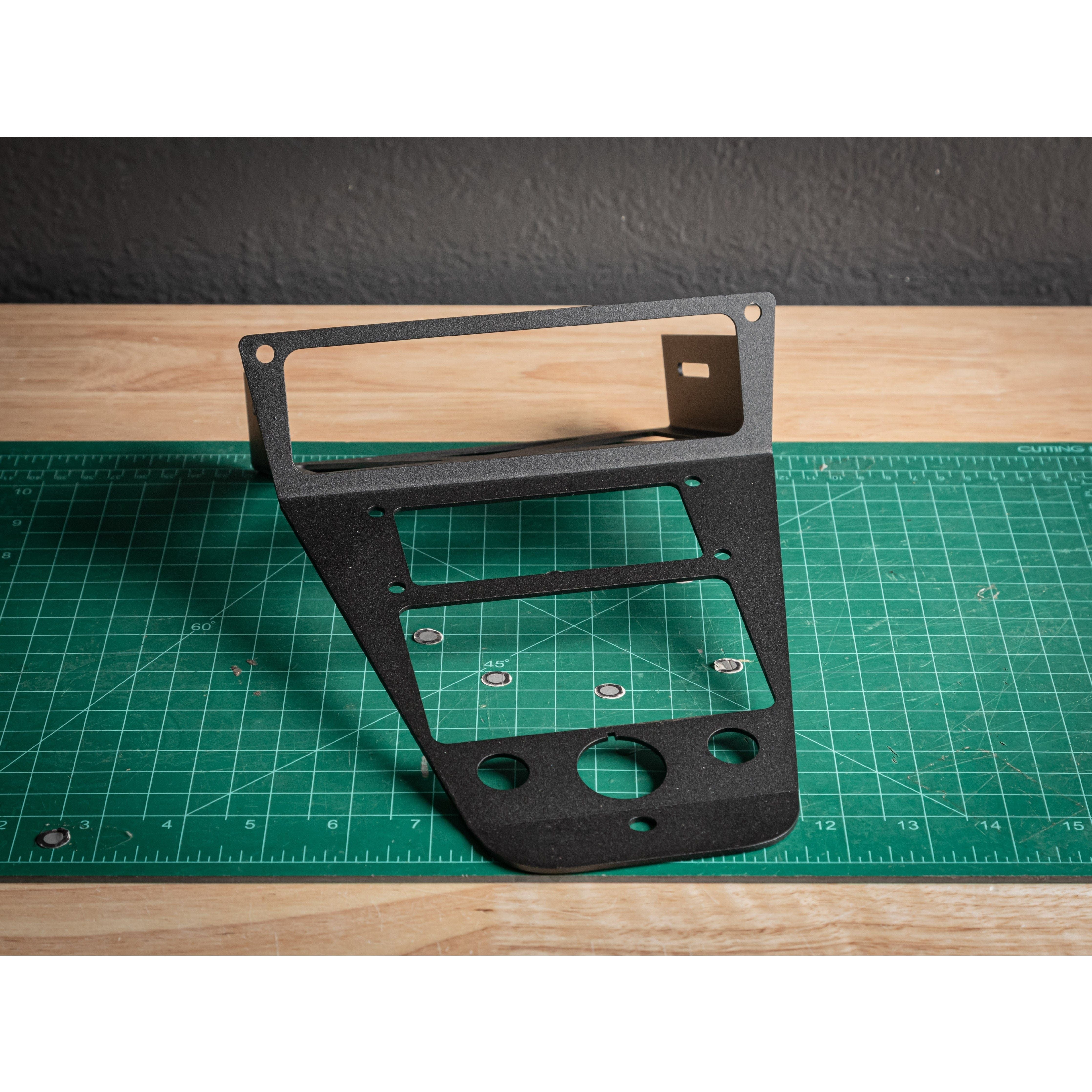 A black Short Polaris ProR/XP Rugged Radios RLB 8 Gang dash panel by StayFlush, compatible with Switchpro 9100, stands upright on a green cutting mat with grid lines atop a wooden surface against a dark wall.