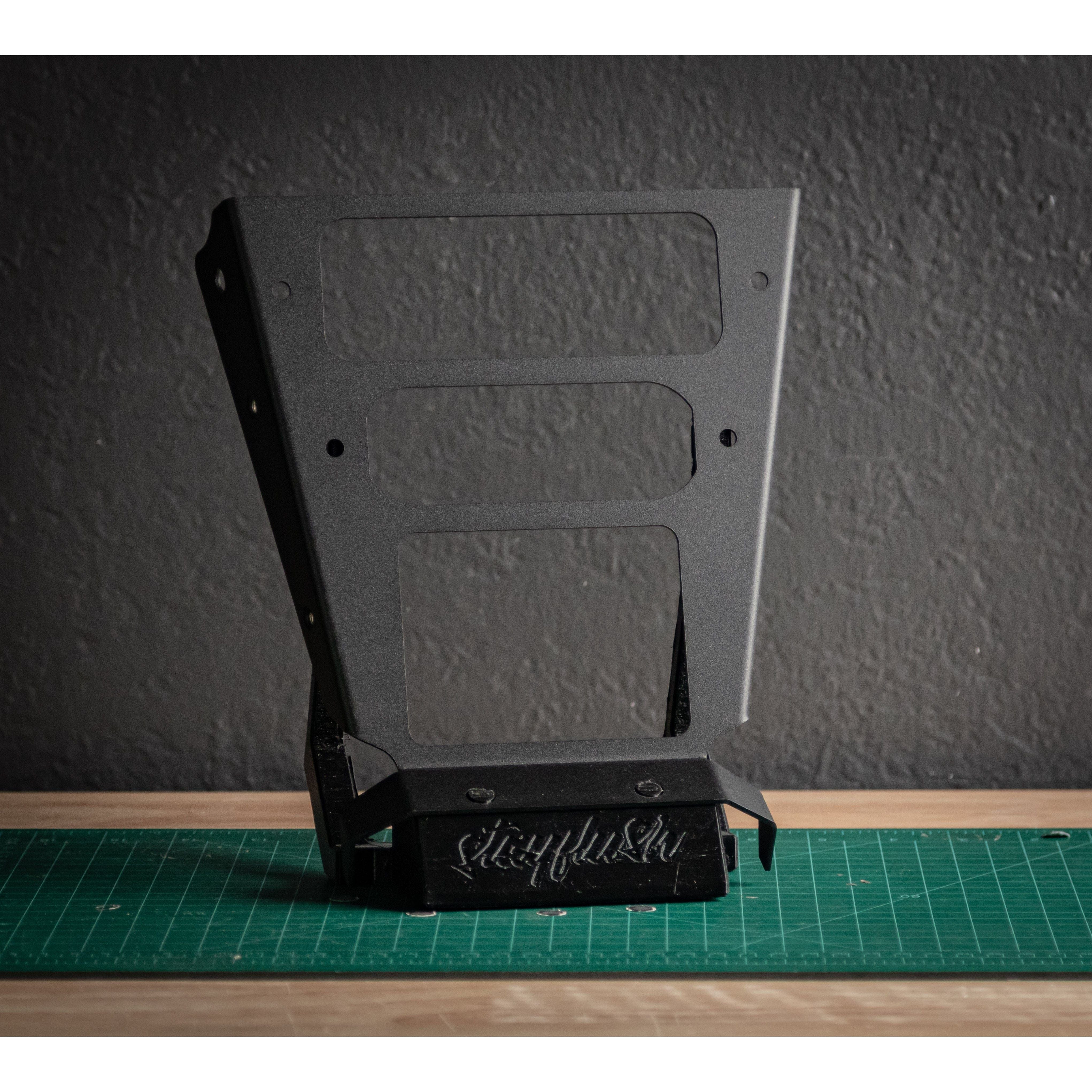 The X3 one off console 0007 by StayFlush is a black metal bracket with rectangular cutouts, shown upright on a green cutting mat. Ideal for mounting devices like the TYT MD-9600, its base features the stylized StayFlush logo.